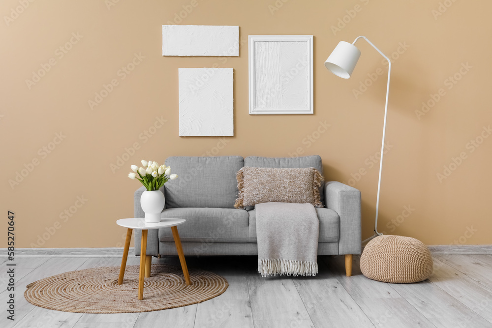 Cozy grey sofa with cushion and vase of tulip flowers on table near beige wall