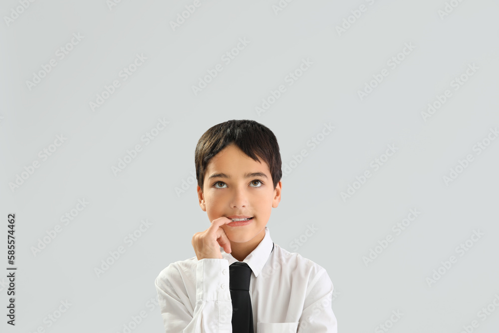 Little schoolboy biting nails on grey background