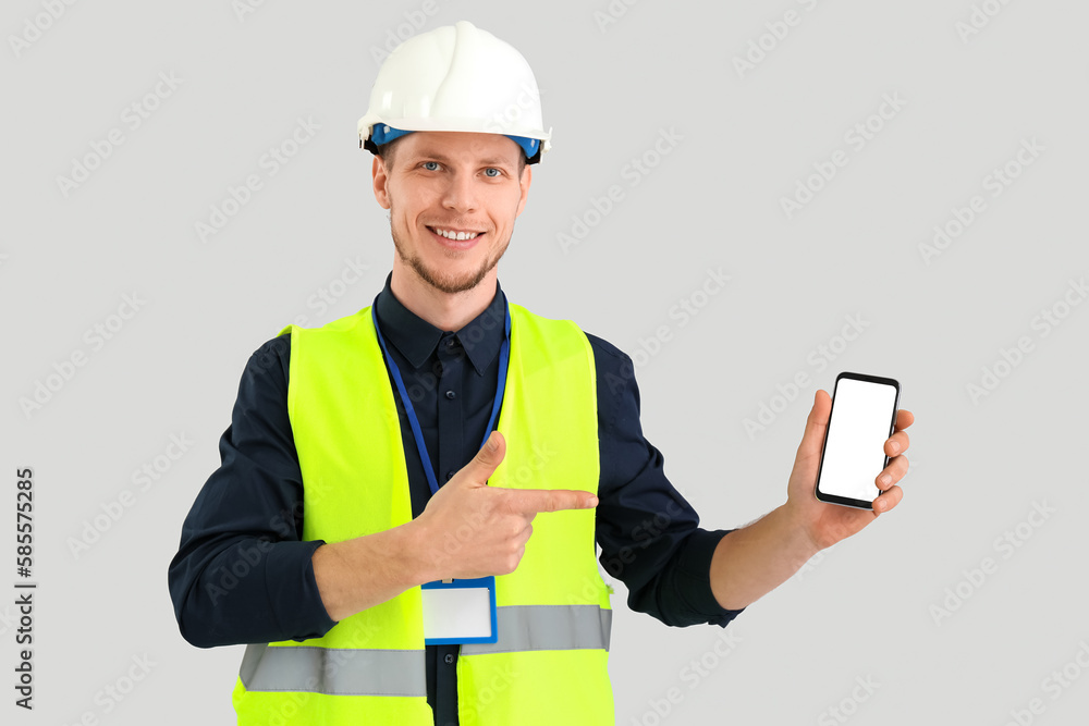 Male worker in vest and with phone on grey background