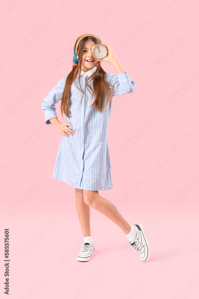 Little girl with alarm clock on pink background