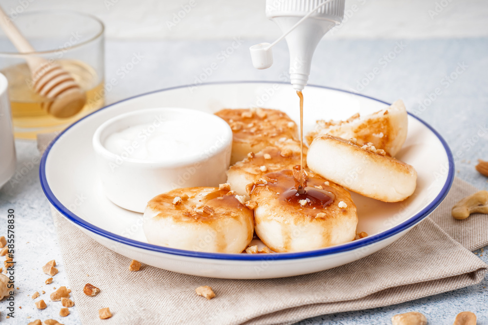 Pouring of caramel syrup onto tasty cottage cheese pancakes on table, closeup