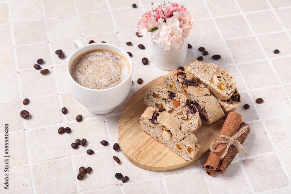 Board with delicious biscotti cookies, cup of coffee, flowers and beans on tile background