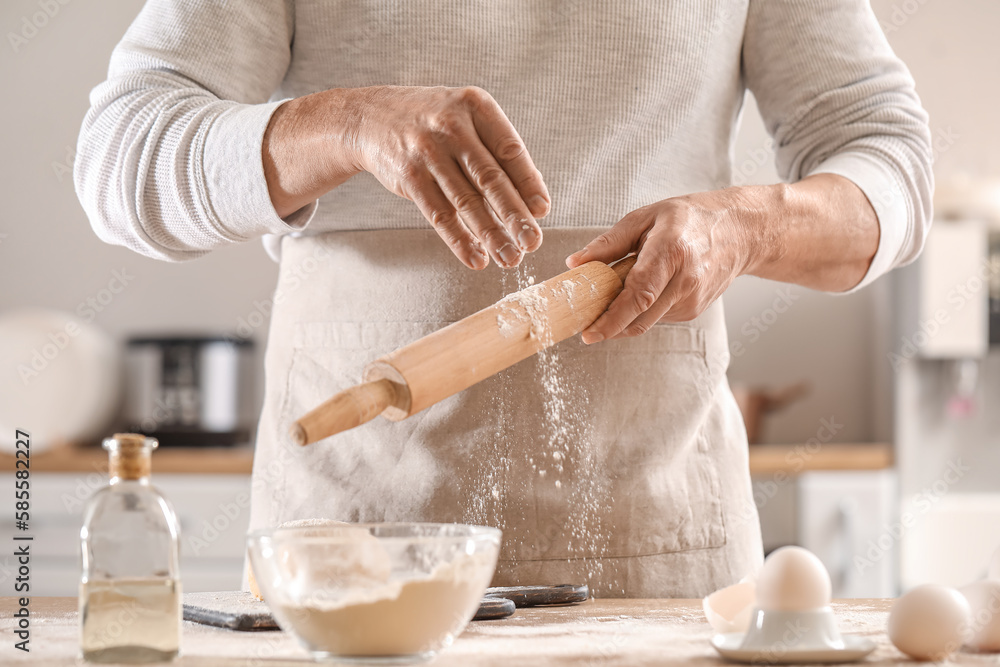 Male chef making dough for pasta at table in kitchen, closeup