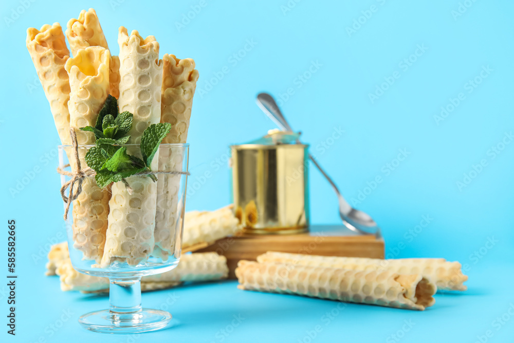 Glass with delicious wafer rolls and mint on blue background