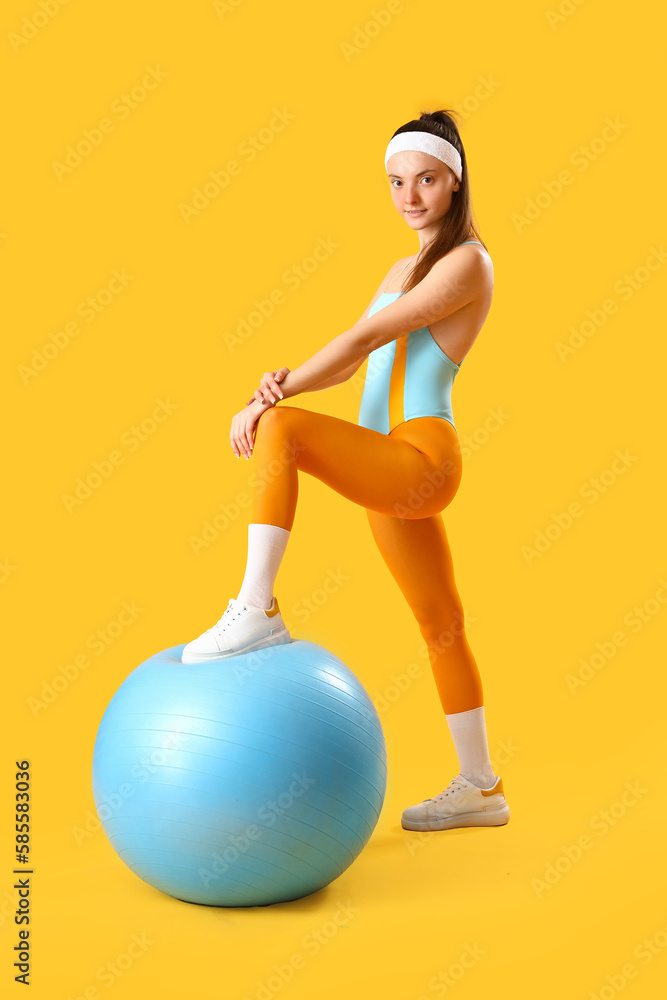 Sporty young woman with fitball on yellow background