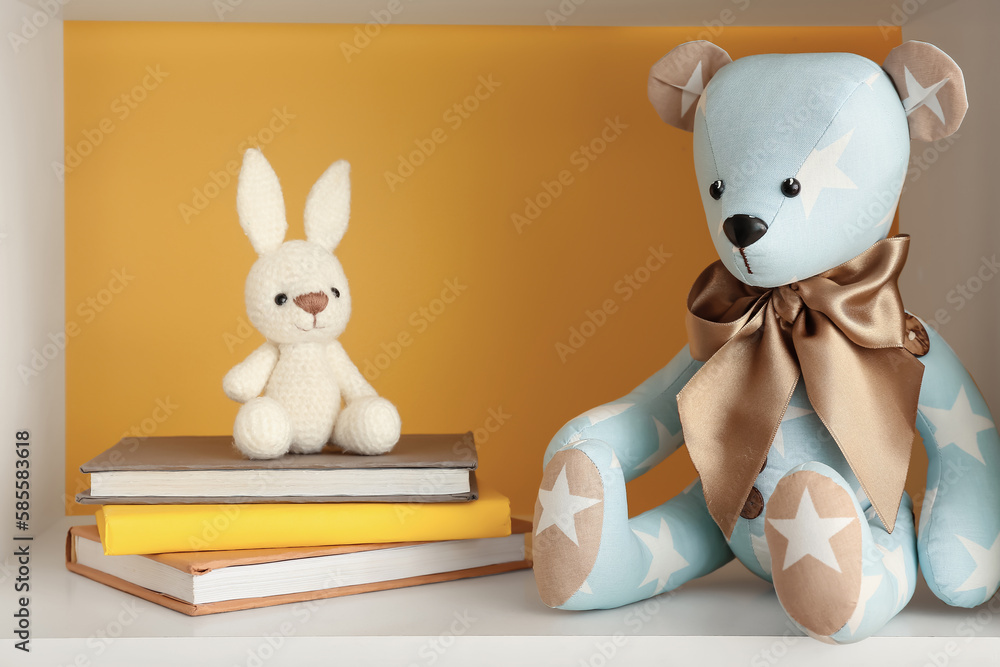 Toy bear and bunny with books on shelf near yellow wall