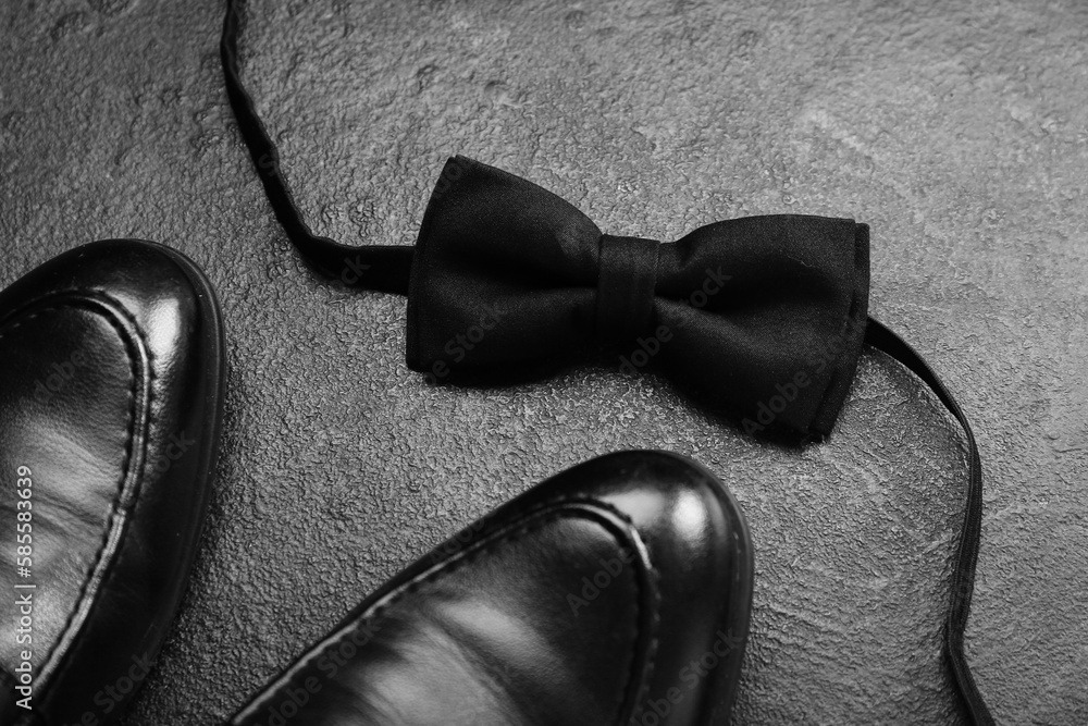 Stylish male shoes and bow tie on dark background, closeup