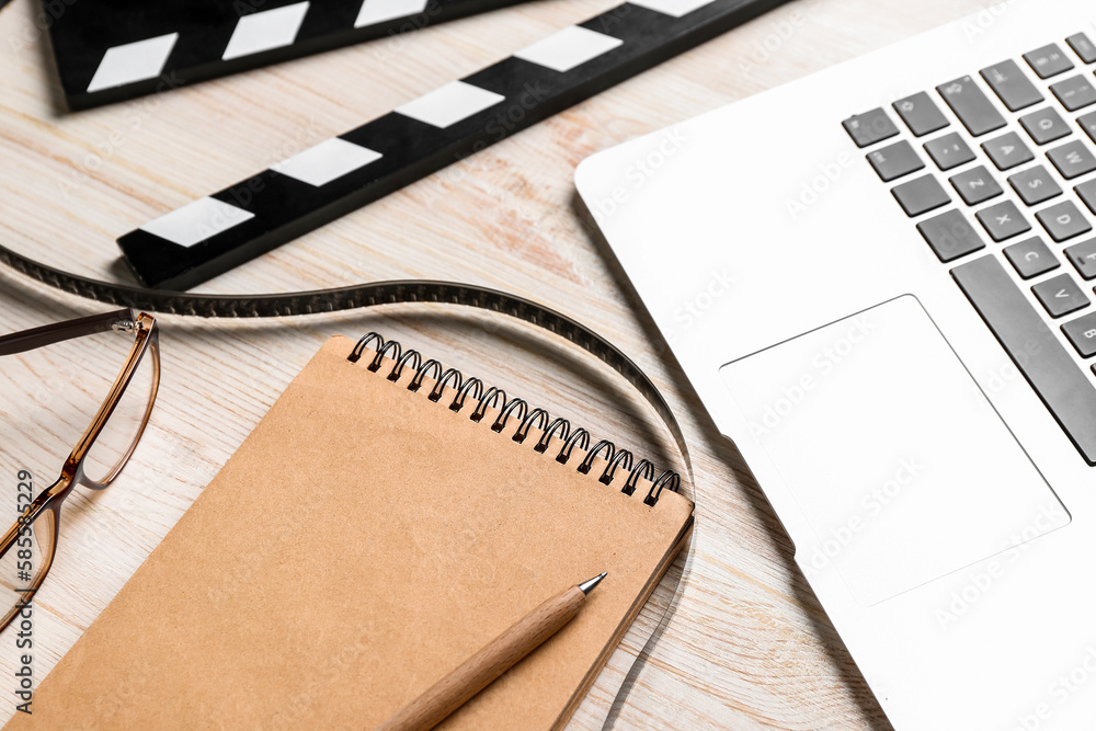 Notebook with film, movie clapper and laptop on light wooden background