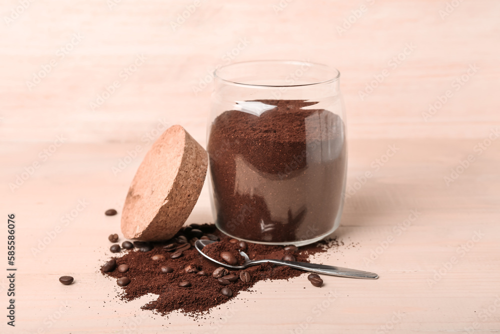 Jar with spoon of coffee powder and beans on light wooden table