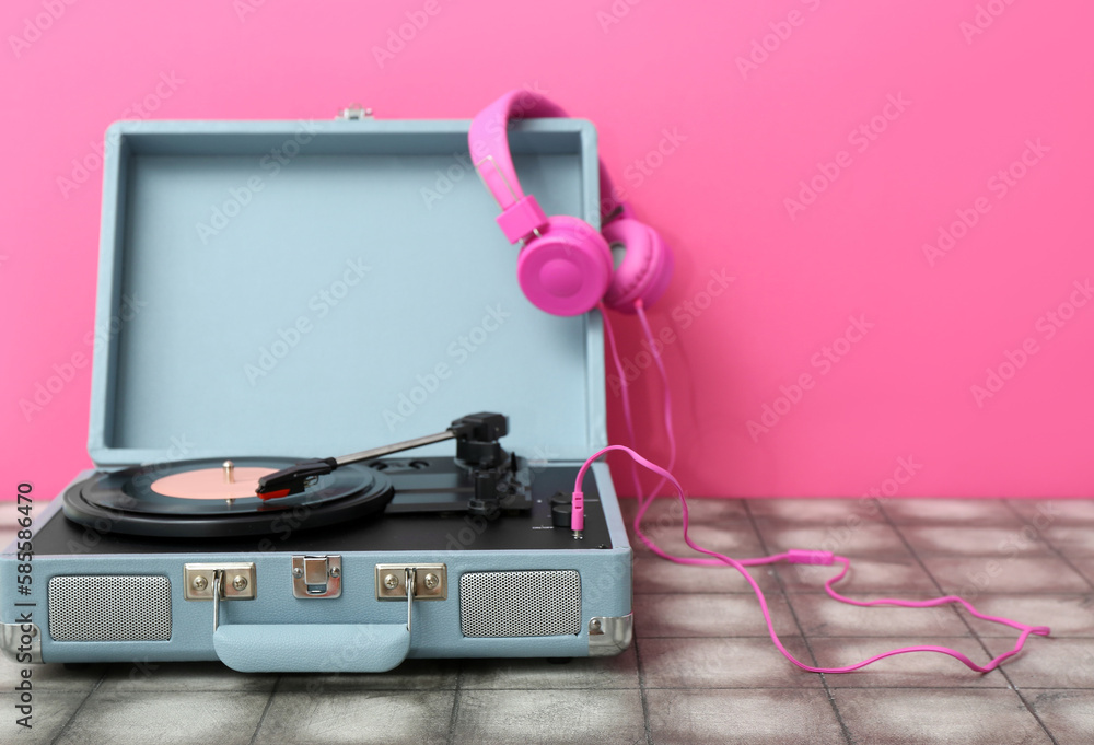 Record player with vinyl disk and headphones on table near pink wall