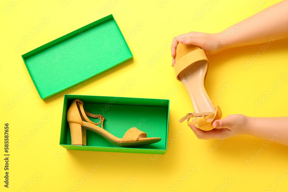 Woman taking stylish shoes out of cardboard box on yellow background