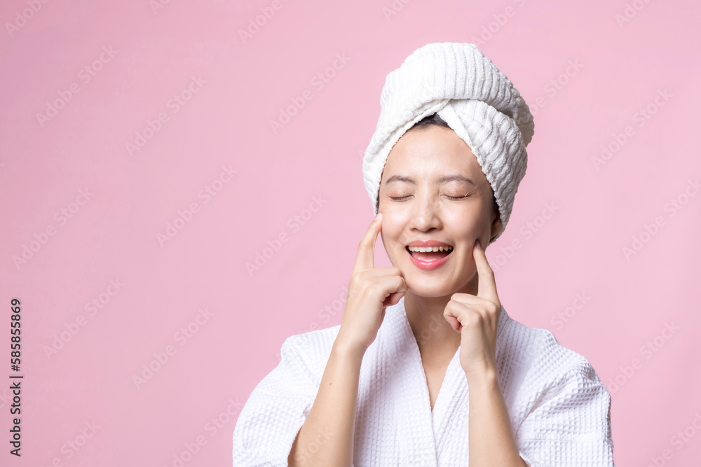 Beautiful young asian woman happy with clean face skin in towel and bathrobe, spa suit on pink backg