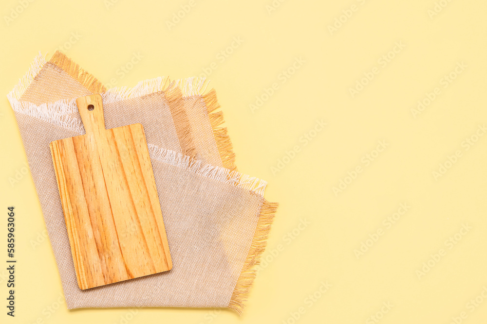 Wooden cutting board and napkin on yellow background