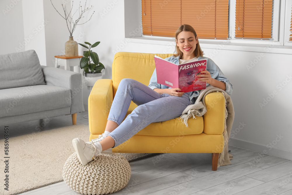 Young woman reading magazine in yellow armchair at home