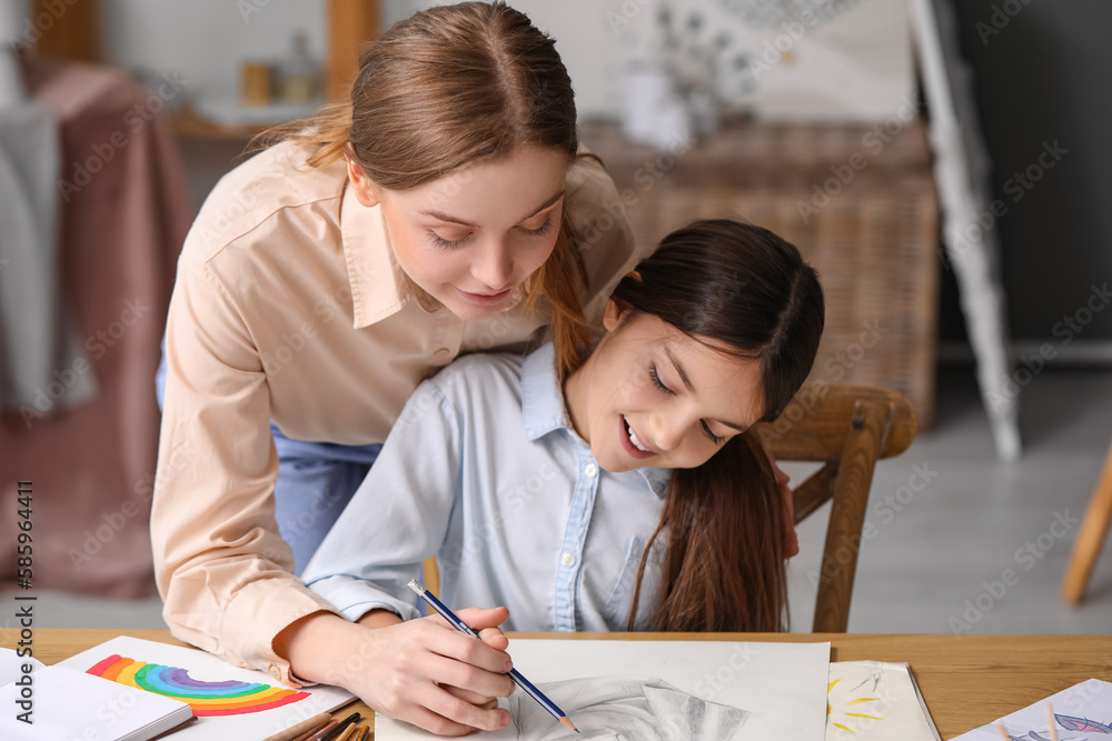 Drawing teacher with pencil giving private art lesson to little girl in workshop