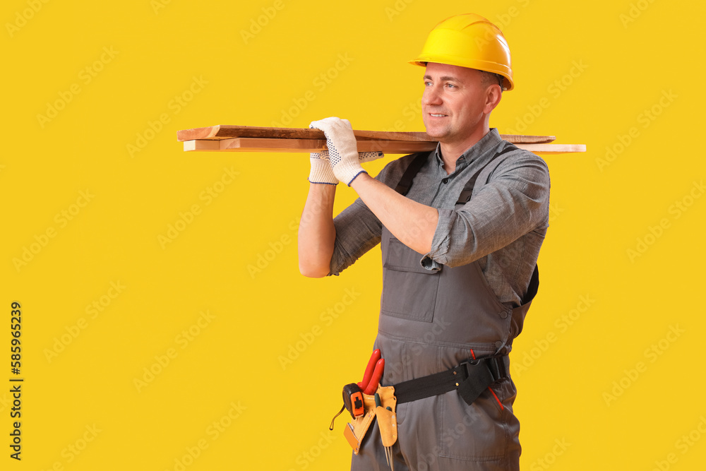 Mature carpenter with wooden planks on yellow background