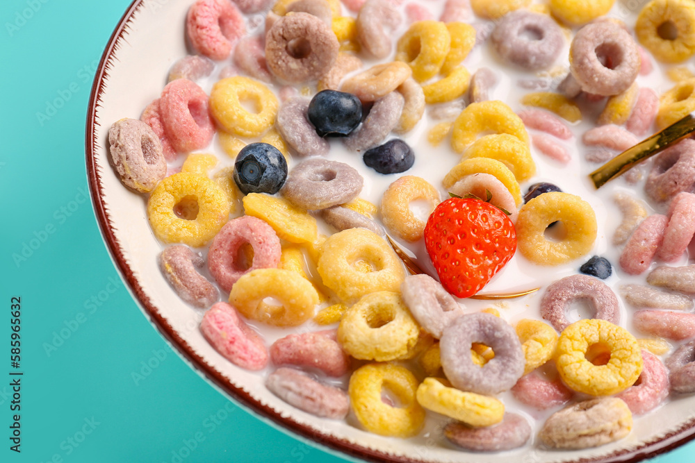 Bowl of colorful cereal rings with milk, strawberry and blueberries on turquoise background