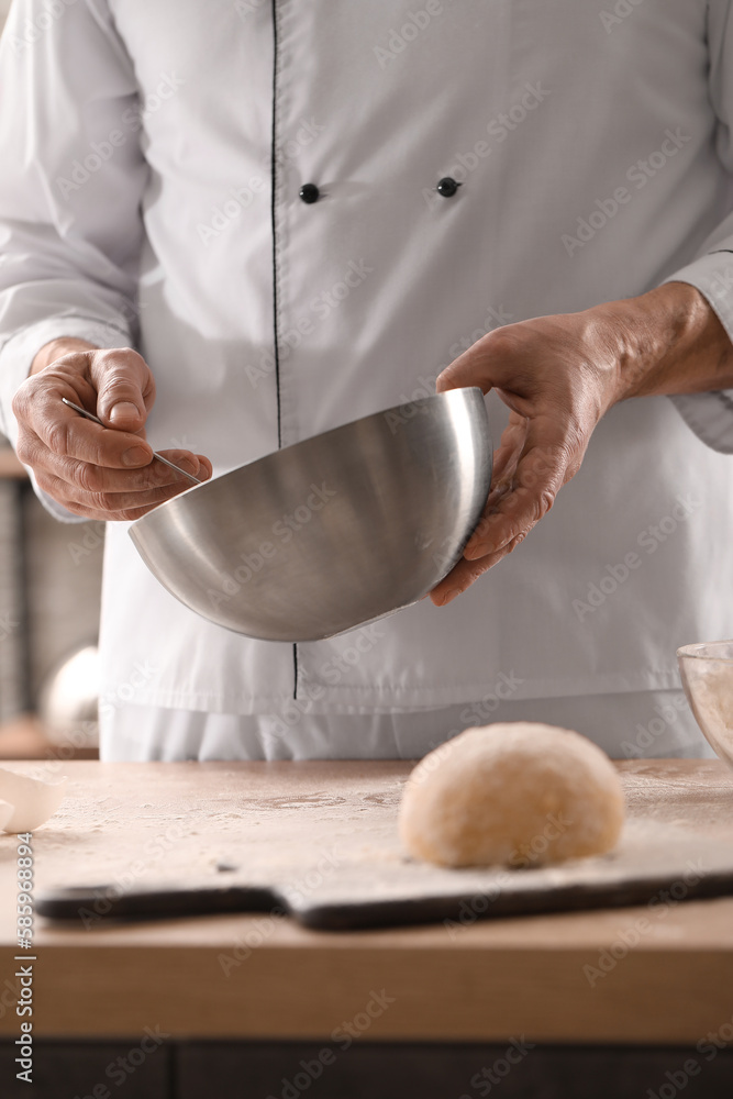 Male chef making dough for pasta at table in kitchen, closeup