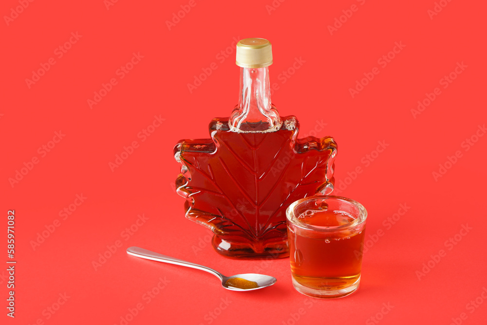 Bottle and glass of tasty maple syrup on red background