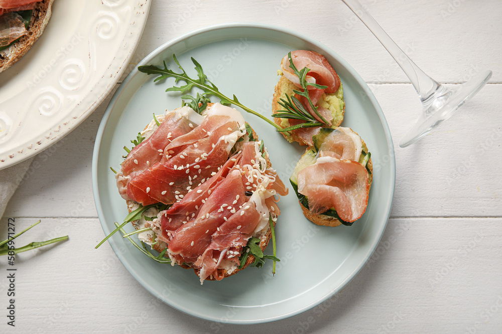 Plate of tasty bruschettas with ham on white wooden background