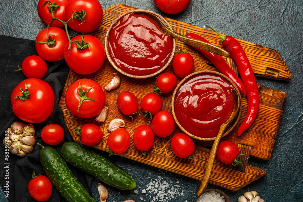 Bowls with tasty ketchup and fresh vegetables on dark background