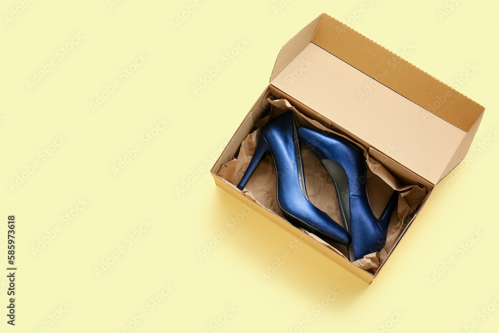 Cardboard box with high heeled shoes on beige background