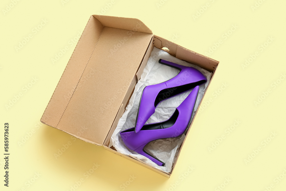 Cardboard box with high heeled shoes on beige background