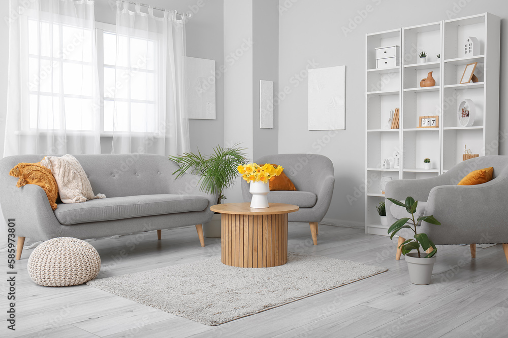 Interior of light living room with cozy sofa, armchairs and flower vase on coffee table