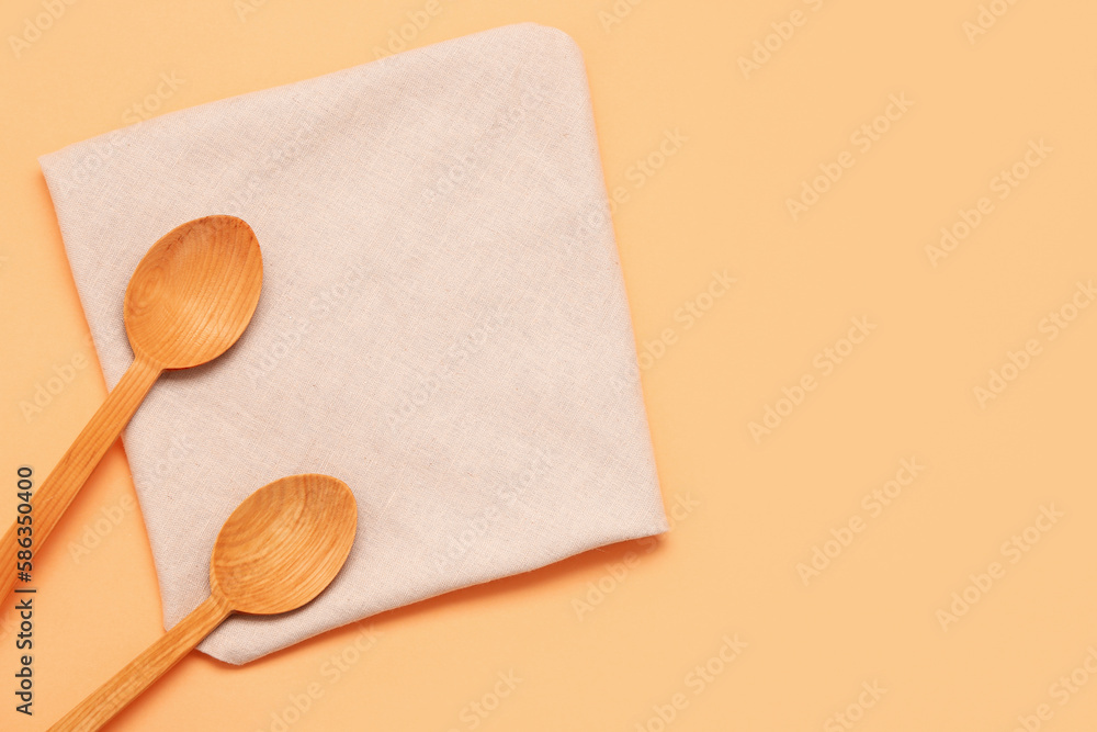 Wooden spoons and folded napkin on color background