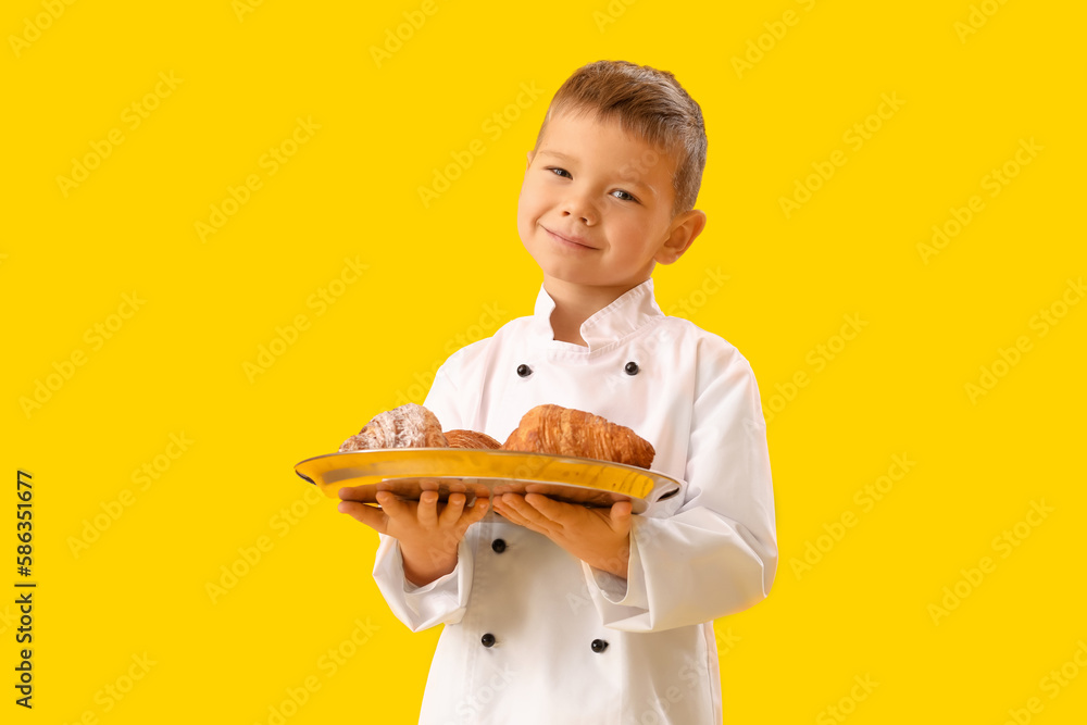 Cute little chef with tray of croissants on yellow background