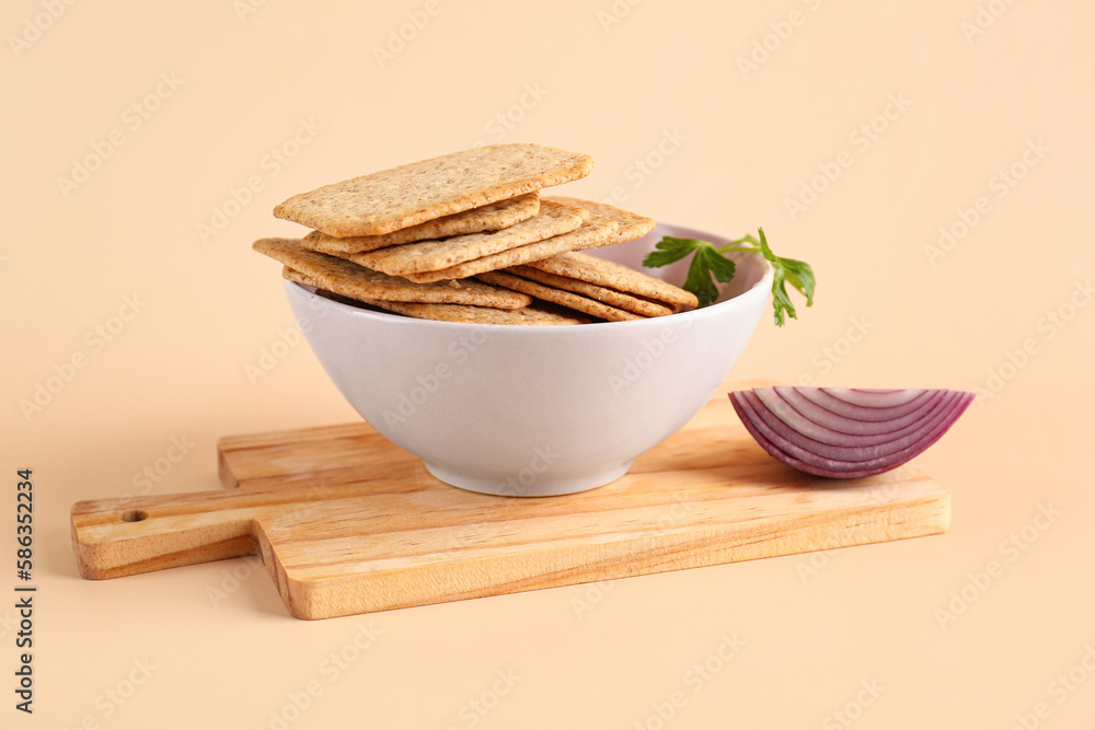 Bowl with tasty crackers, parsley and onion on beige background