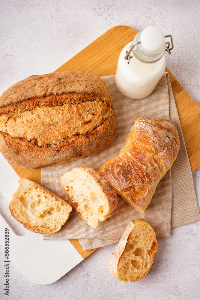 Board with slices of fresh bread and bottle of milk on white background