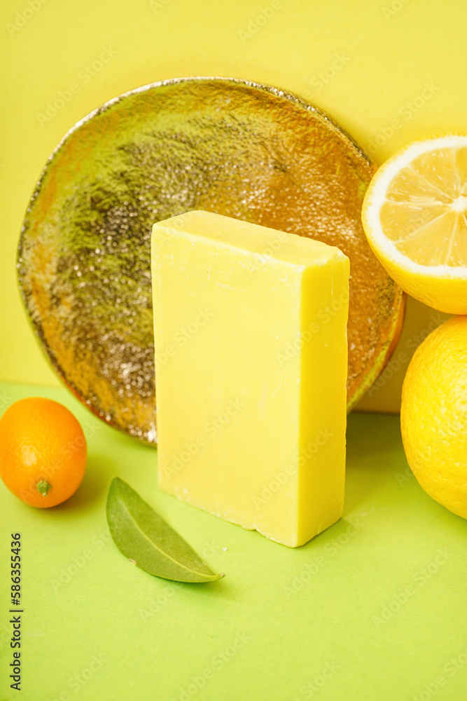 Composition with natural soap bar, golden plate and citrus fruits on color background, closeup