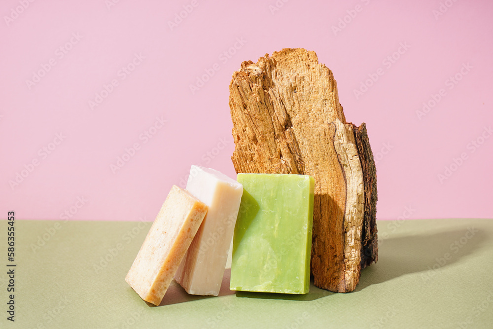 Natural soap bars and tree bark on color background