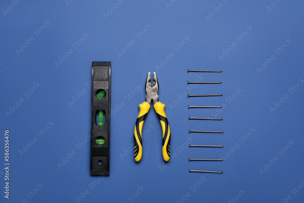 Pliers, level and nails on blue background