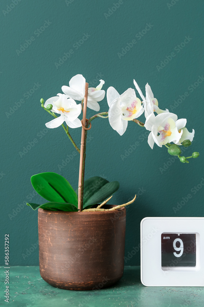 Artificial flower with clock on table near green wall