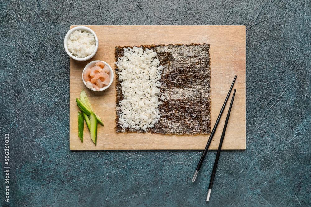 Wooden board with nori and ingredients for preparing sushi rolls on dark background