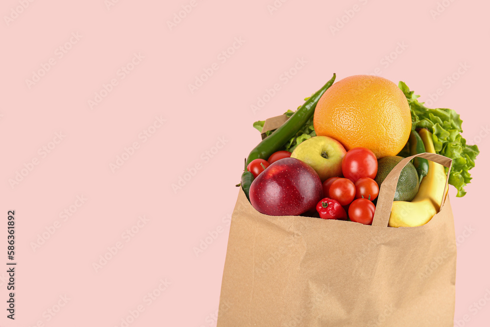 Paper bag with vegetables and fruits on pink background