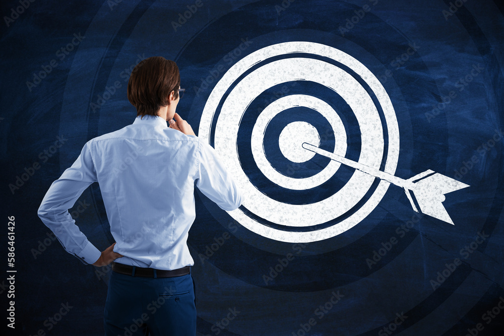 Back view of thoughtful young businessman looking at hand drawn target and arrow on blue background.