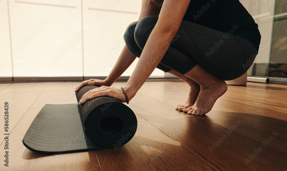 Unrecognizable senior woman rolling up an exercise mat at home