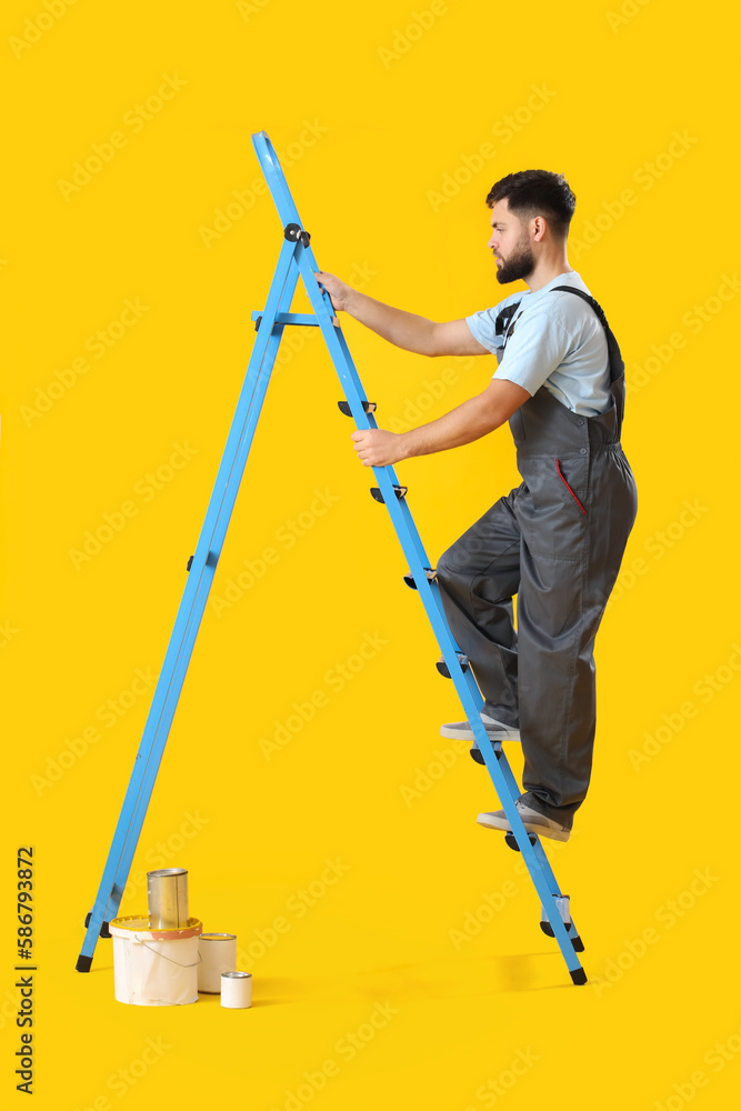 Male worker with ladder and cans of paint on yellow background