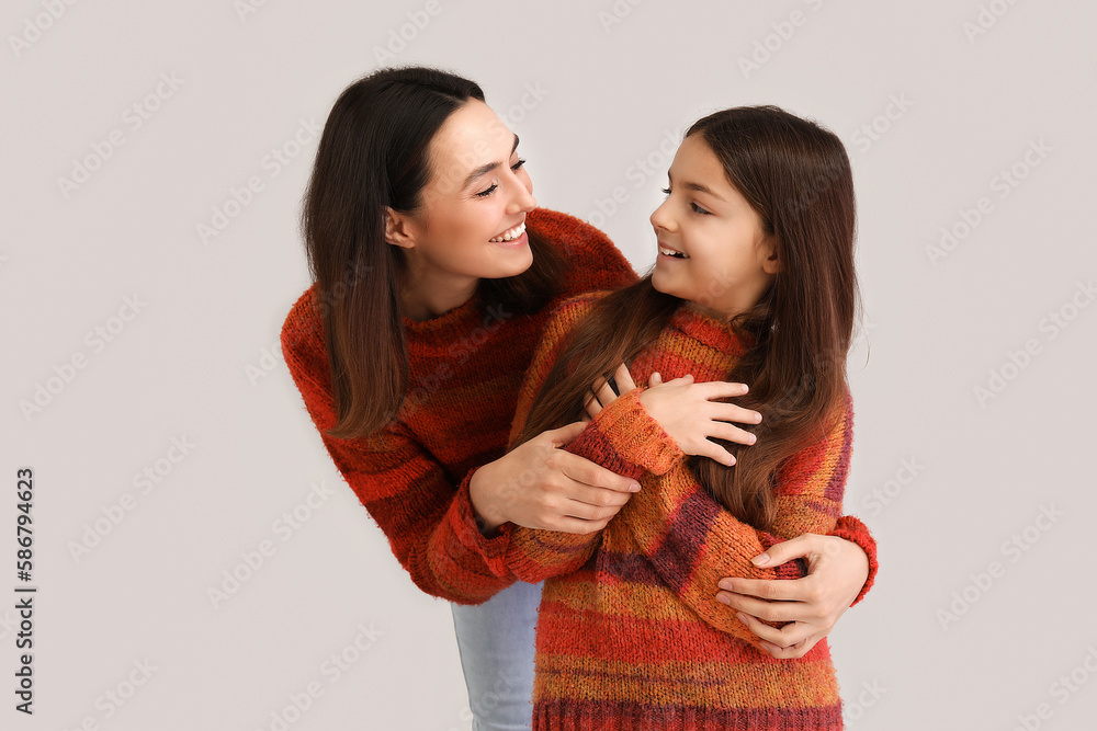 Little girl and her mother in warm sweaters hugging on grey background