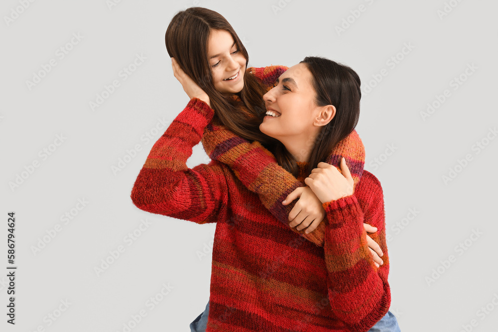 Little girl and her mother in warm sweaters hugging on grey background