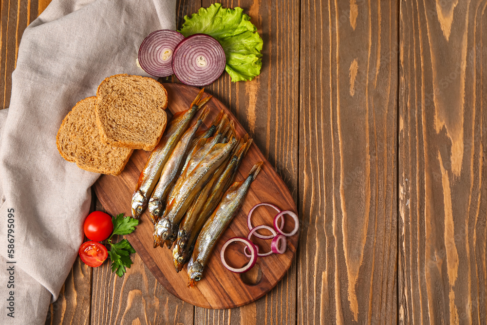 Board with delicious smoked capelin, vegetables and bread on wooden background