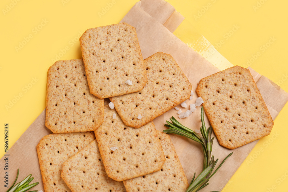 Parchment with tasty crackers, rosemary and salt on yellow background