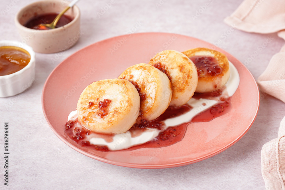 Plate with tasty cottage cheese pancakes, sour cream and raspberry jam on light background