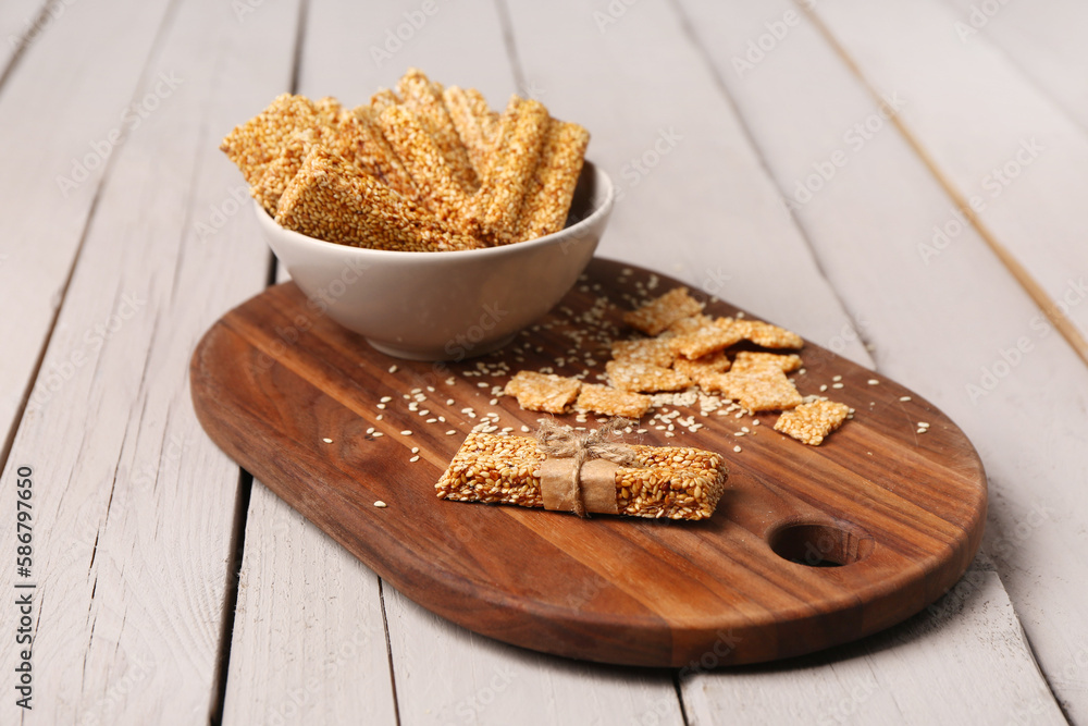 Board with bowl of tasty sesame kozinaki on light wooden background