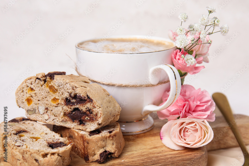 Board with cup of coffee, delicious biscotti cookies and beautiful flowers on white table