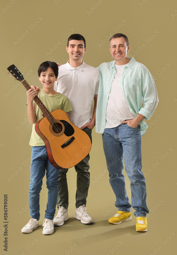 Happy little boy with his dad and grandfather playing guitar on green background