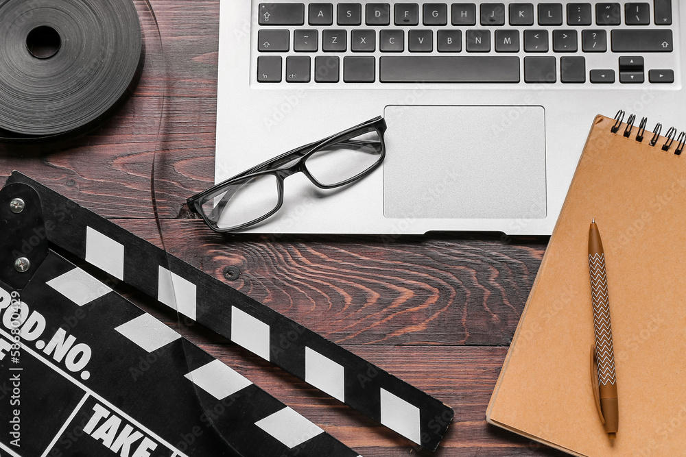 Notebook with laptop, film and movie clapper on dark wooden background